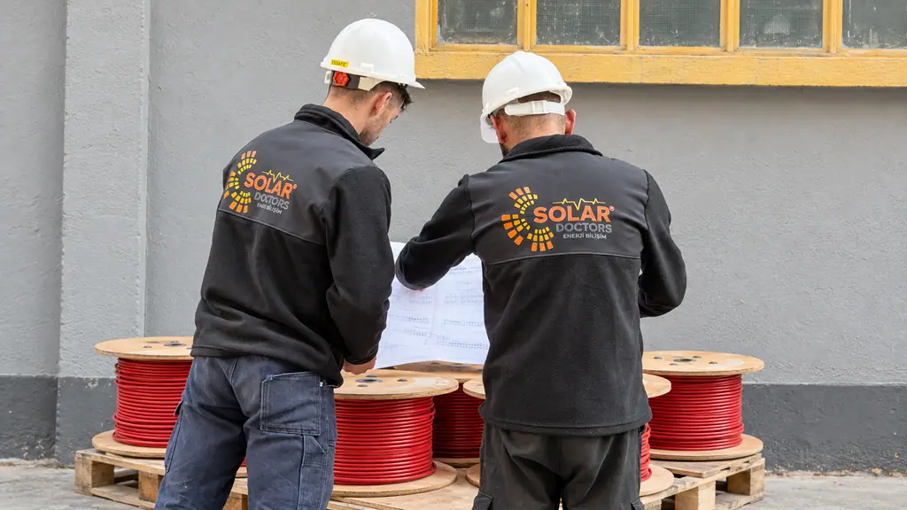 Solar kablo makaraları önünde proje çizimlerini inceleyen iki Solar Doctors çalışanı